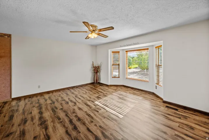 Wood-finish flooring throughout, bay windows with natural wood blinds, ceiling fan with integrated lighting, and neutral wall tones