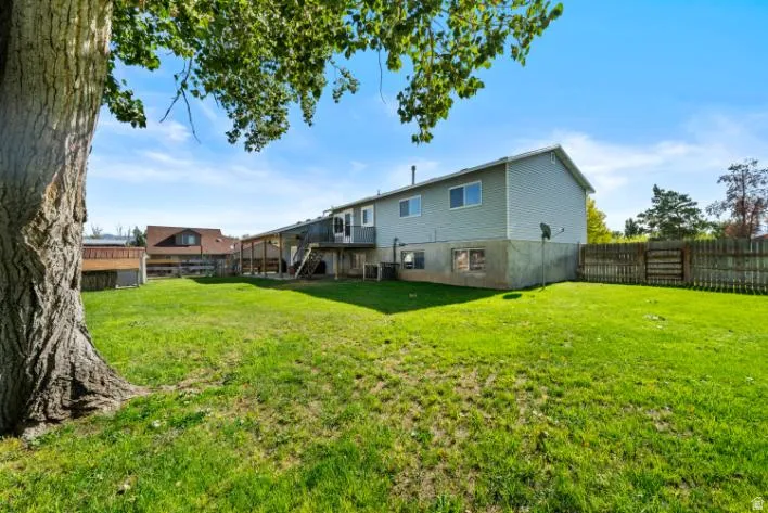 Expansive lawn area, mature tree, multi-level deck, fenced perimeter, and wood siding on the upper level