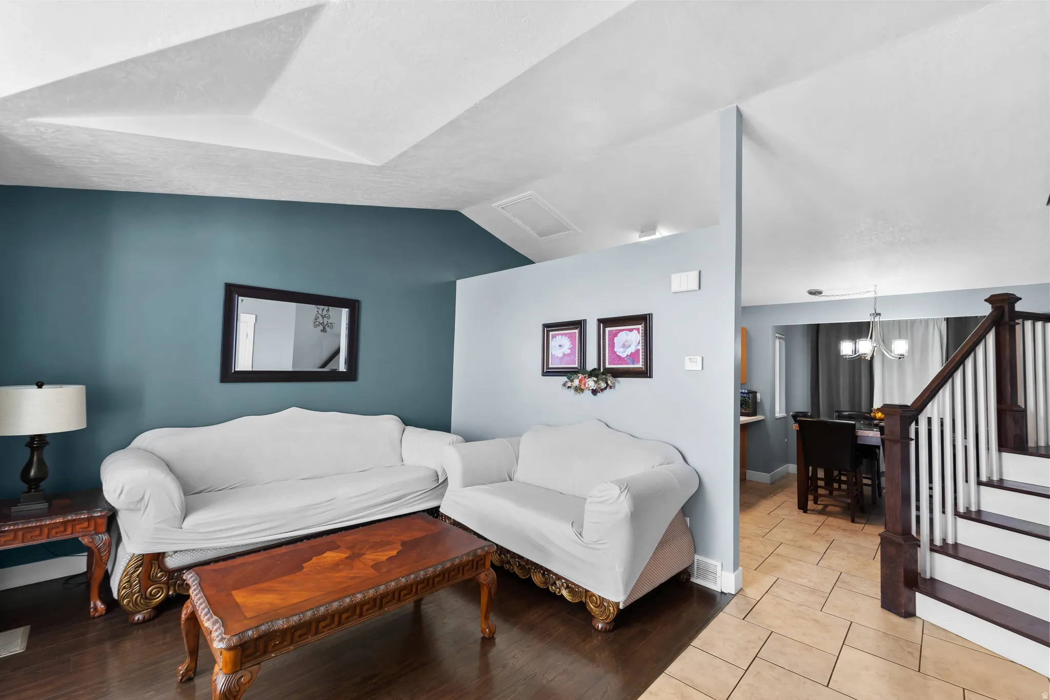 Hardwood-finish flooring, accent wall, staircase with wood newel post and balusters, tiled flooring, and tray ceiling