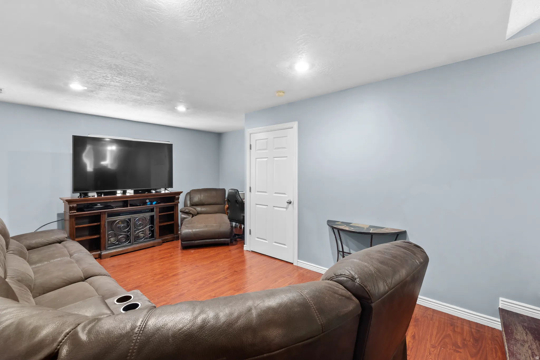Recessed lighting, wood-finish flooring, light blue wall paint, white trim, and a built-in media console