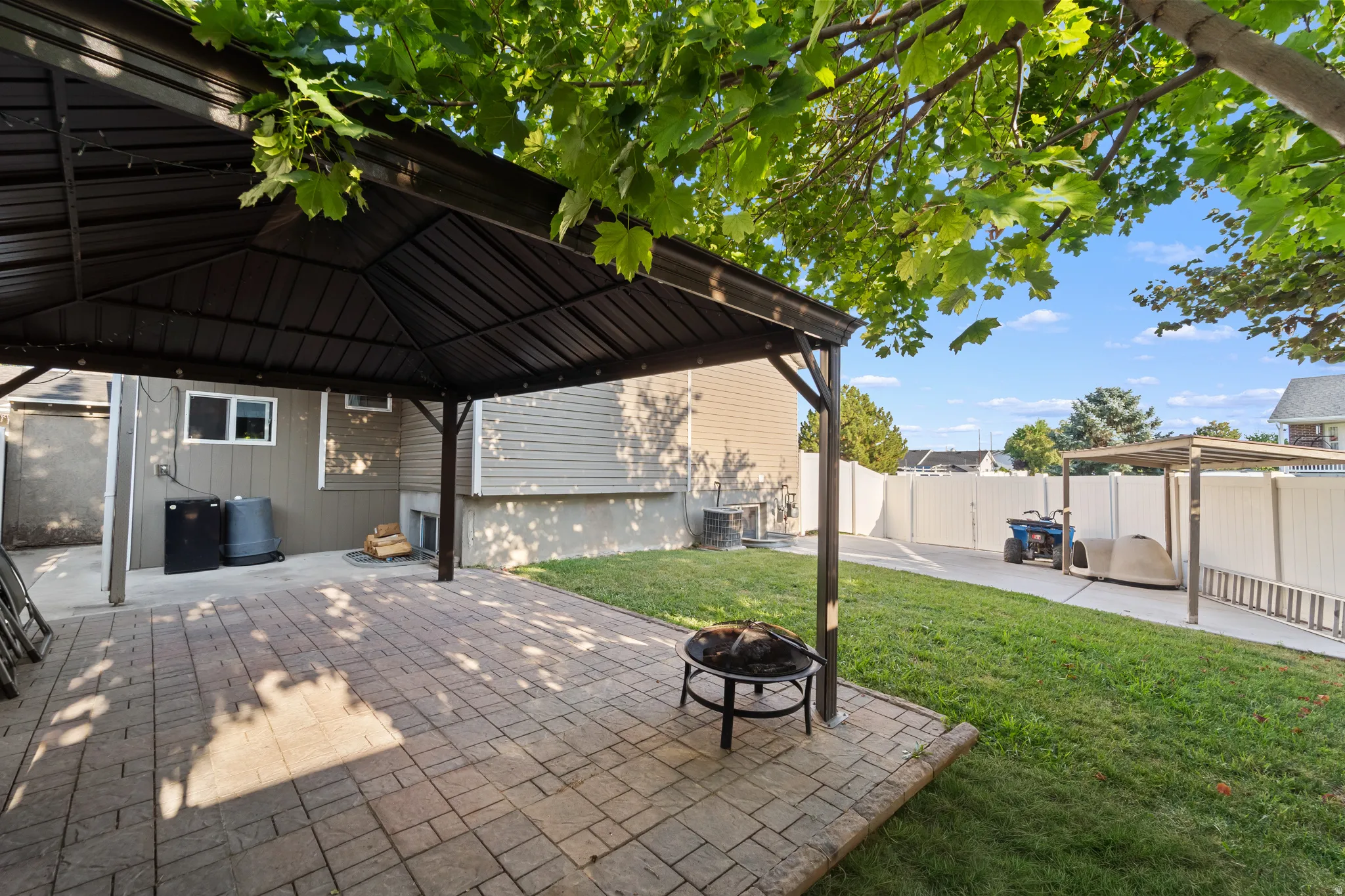 Paved patio with a permanent gazebo structure, expansive lawn, and white privacy fencing