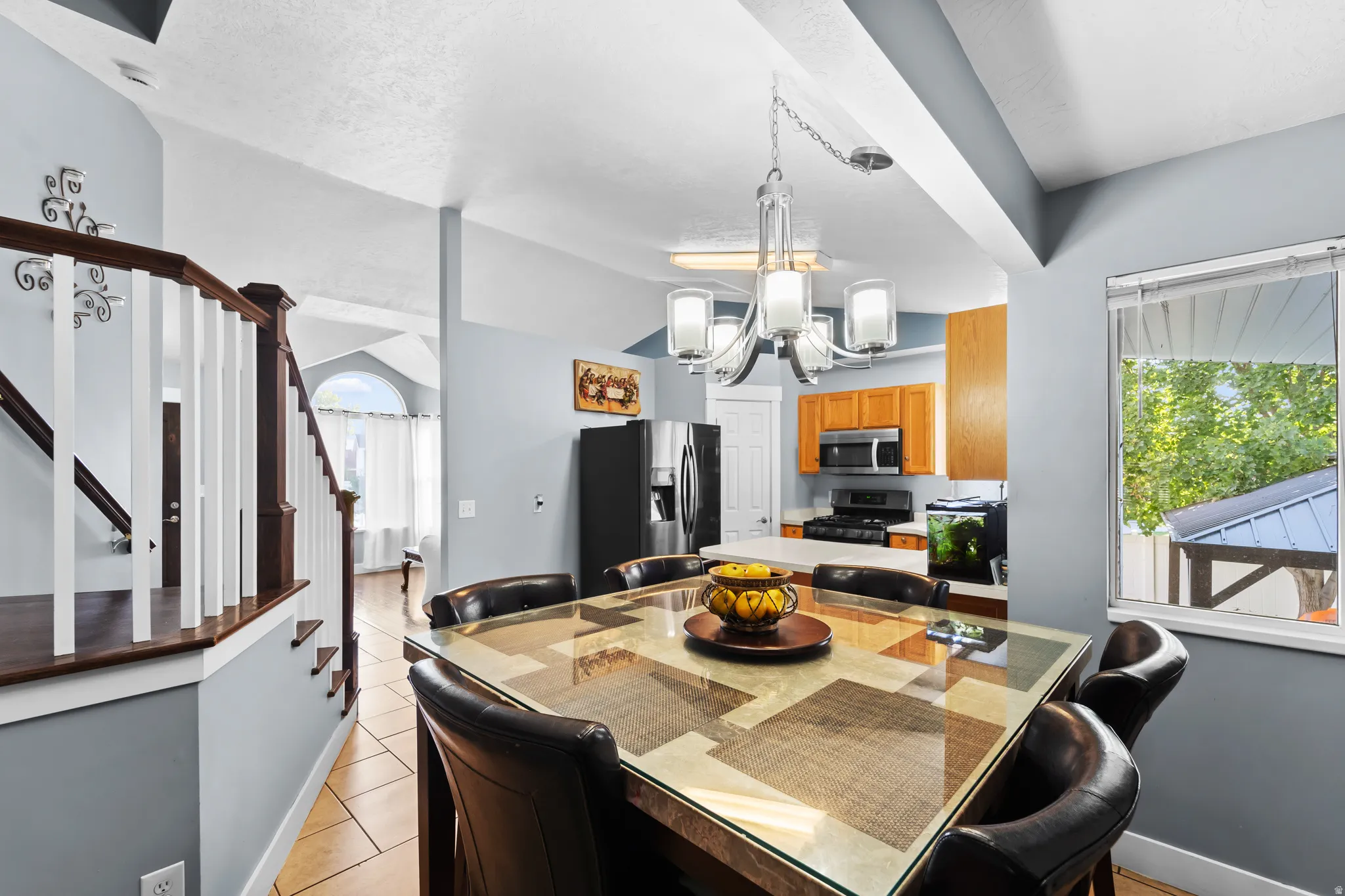 Open concept living with tile flooring, a staircase featuring a wood-finish handrail and white balusters, and a kitchen with wood-finish cabinetry and stainless-steel appliances