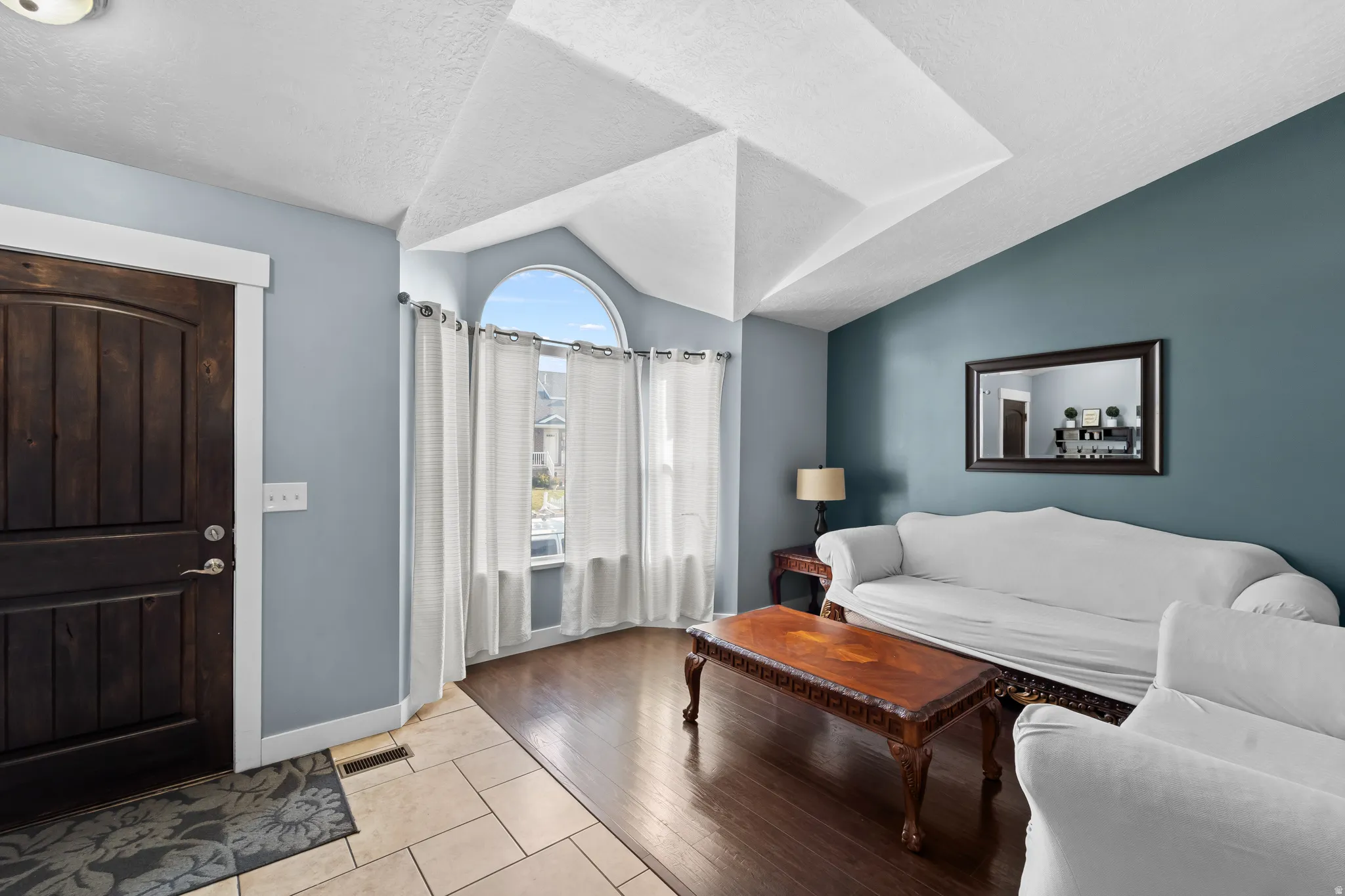 Vaulted ceiling with geometric detail, dark wood-finish flooring, and arched window