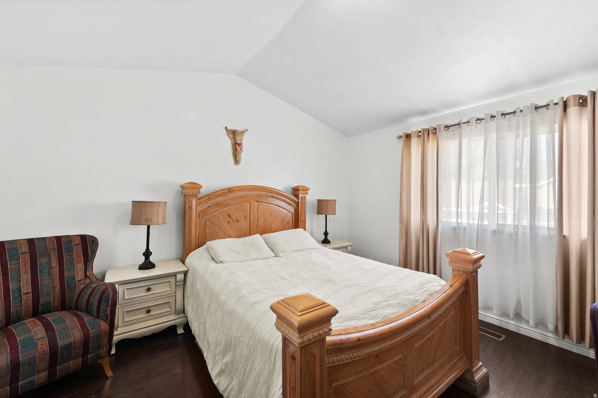 Vaulted ceiling with an overhead light fixture, large window with curtain rod and drapes, wood-finish flooring, and white walls
