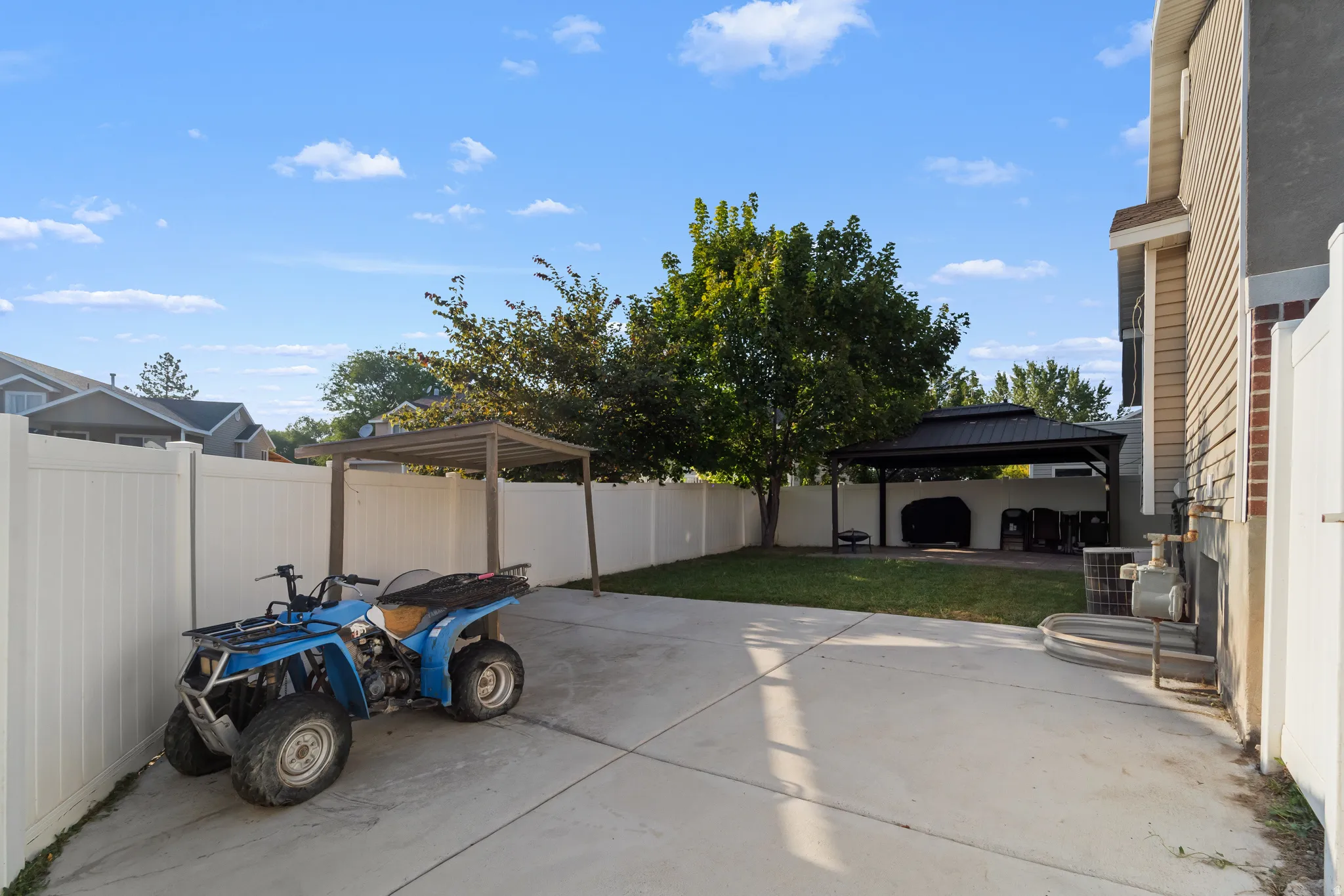 Fenced backyard featuring concrete paving, a covered pergola, mature trees, and a spacious lawn area