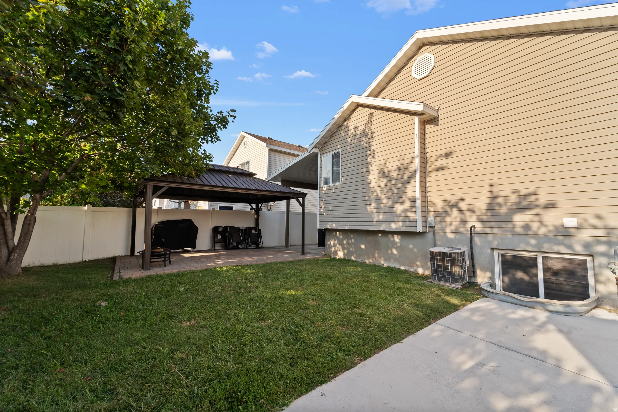 Private backyard featuring a paved patio with a built-in gazebo, established lawn, and a light-colored privacy fence