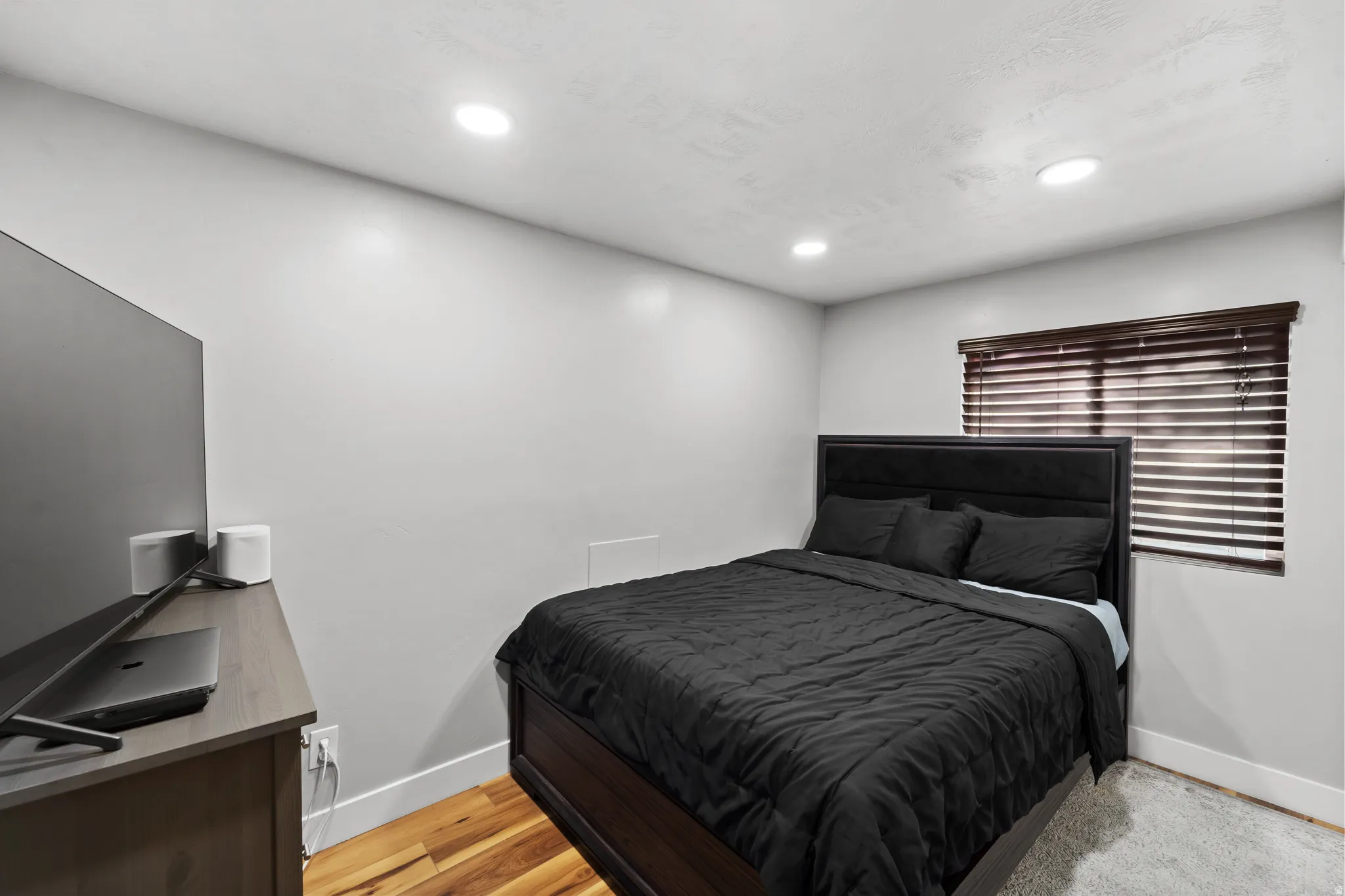 Recessed ceiling lighting, wood-finish flooring, window with horizontal blinds, and a built-in wall vent