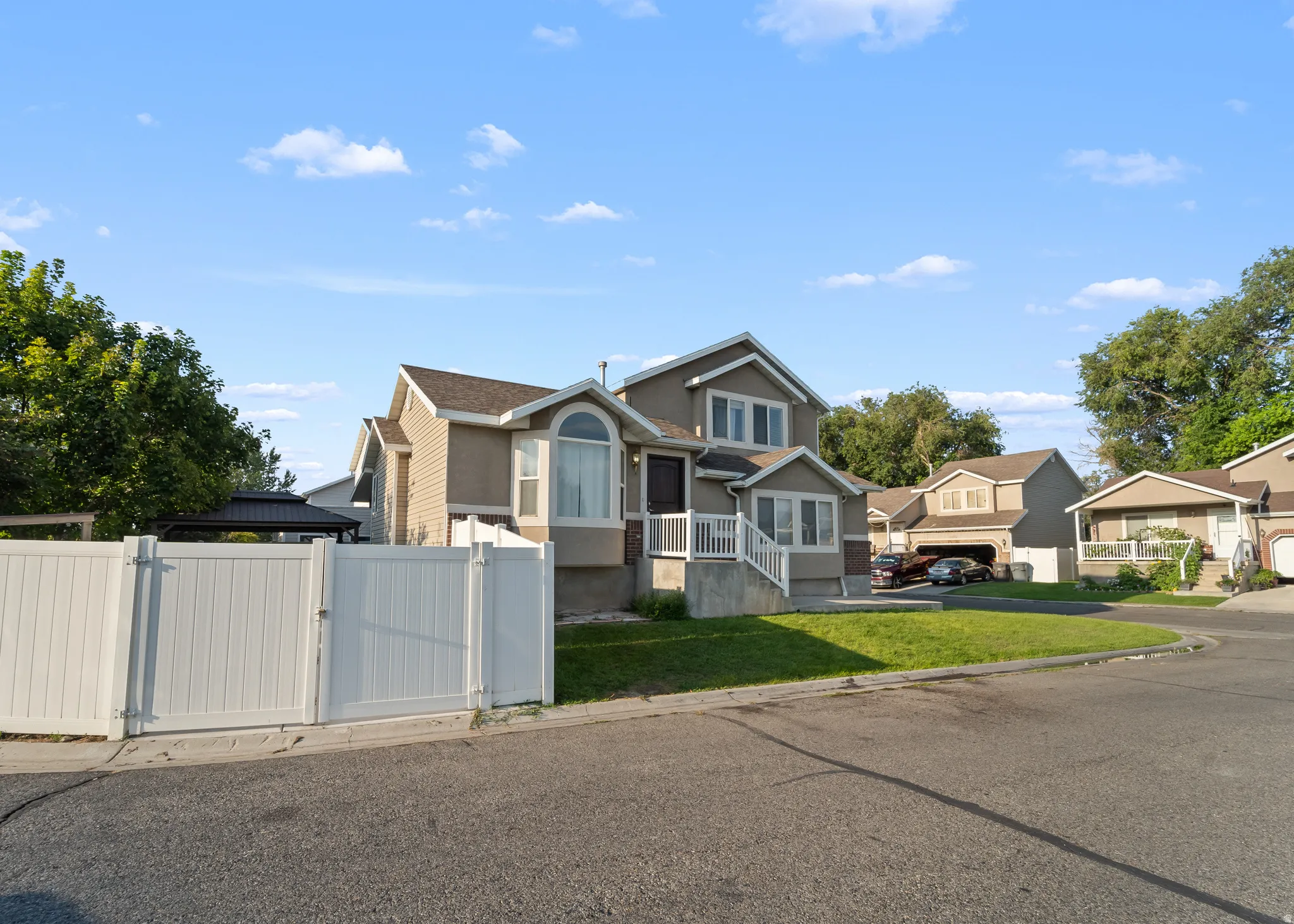 Split-level home featuring a light brown exterior with white trim, an arched window, a white porch railing, and a private fence with a gate