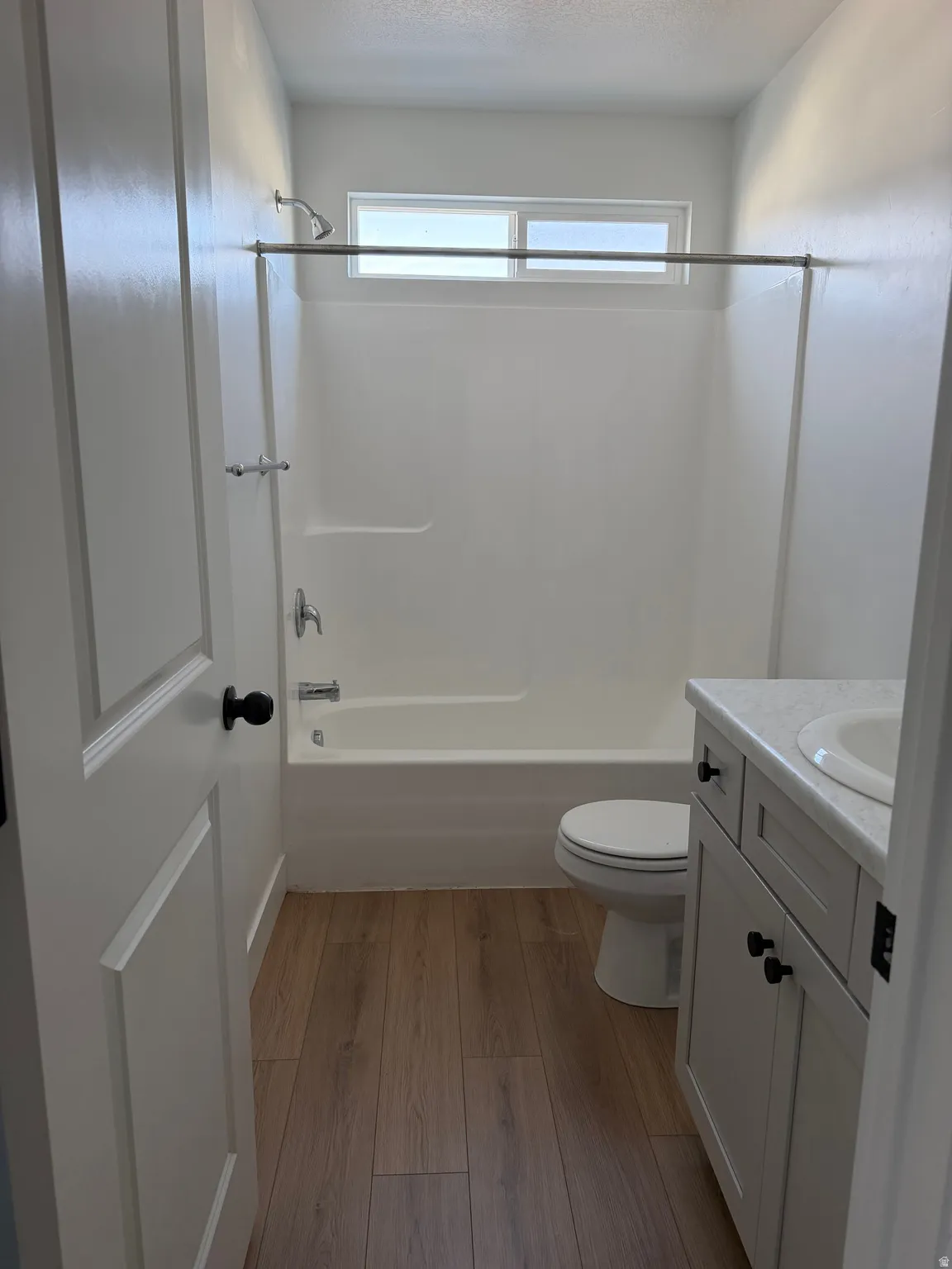 Bright and functional bathroom featuring a wood-finish plank floor, white cabinetry with black hardware, and a ceramic vessel sink