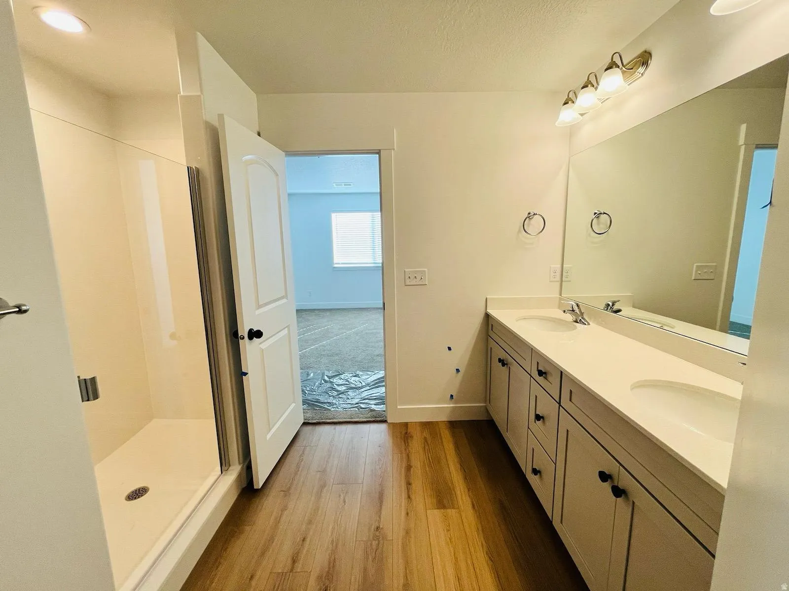 Bathroom featuring a dual vanity with light-toned cabinetry, a spacious mirror, and a shower enclosure