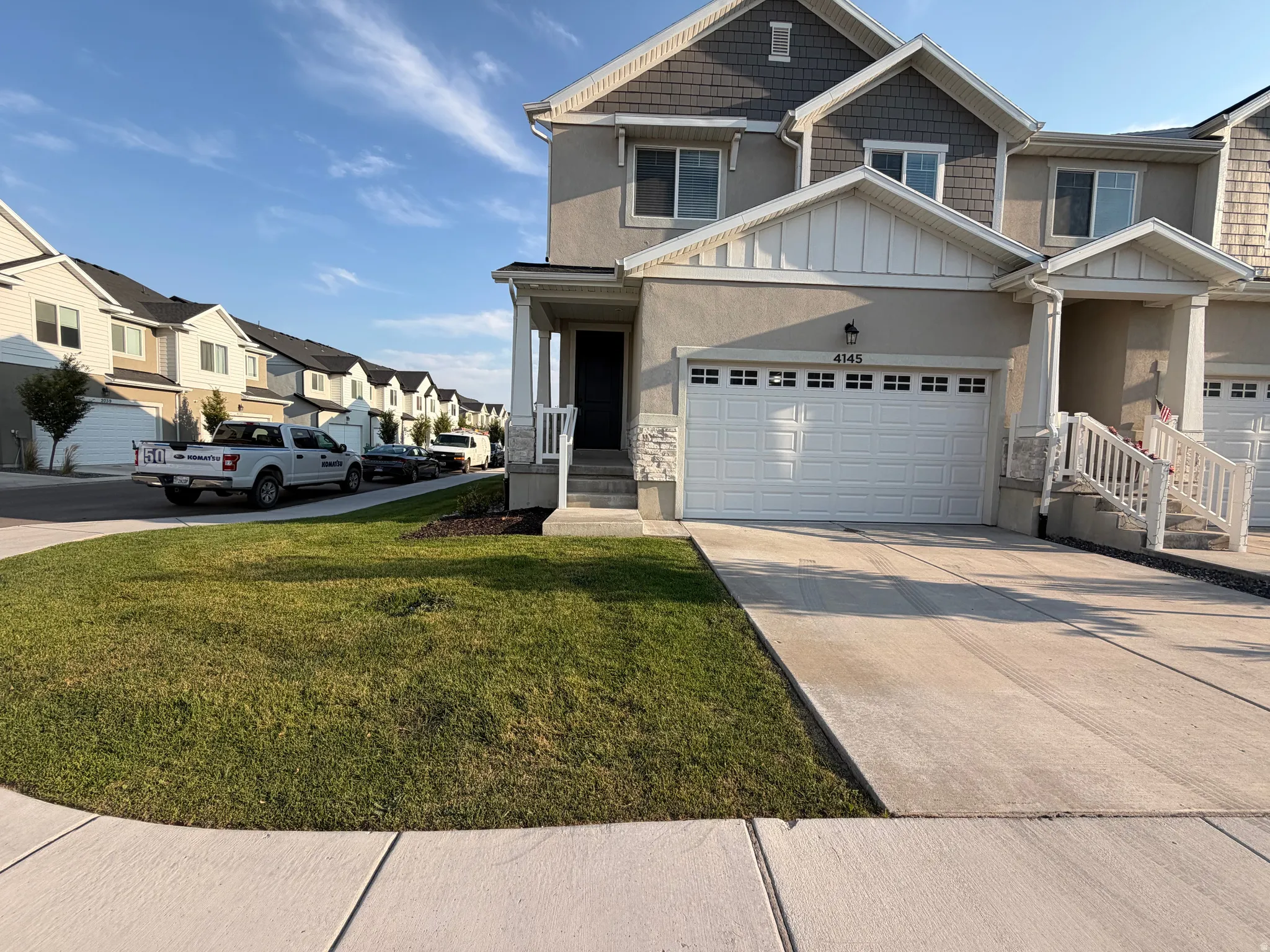 Welcoming two-car garage with white paneled doors anchors this two-story home, complemented by a manicured front lawn, concrete driveway, and established landscaping