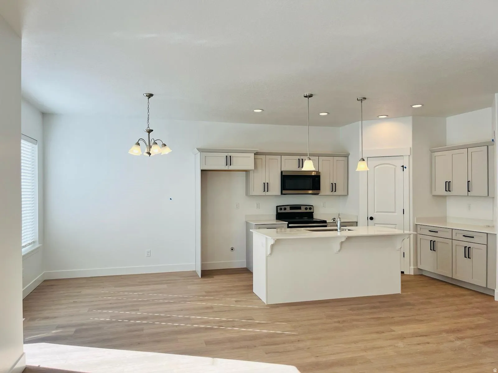 Open-concept kitchen and dining area featuring light wood-finish flooring, a kitchen island with pendant lighting, white cabinetry with dark hardware, and a built-in microwave