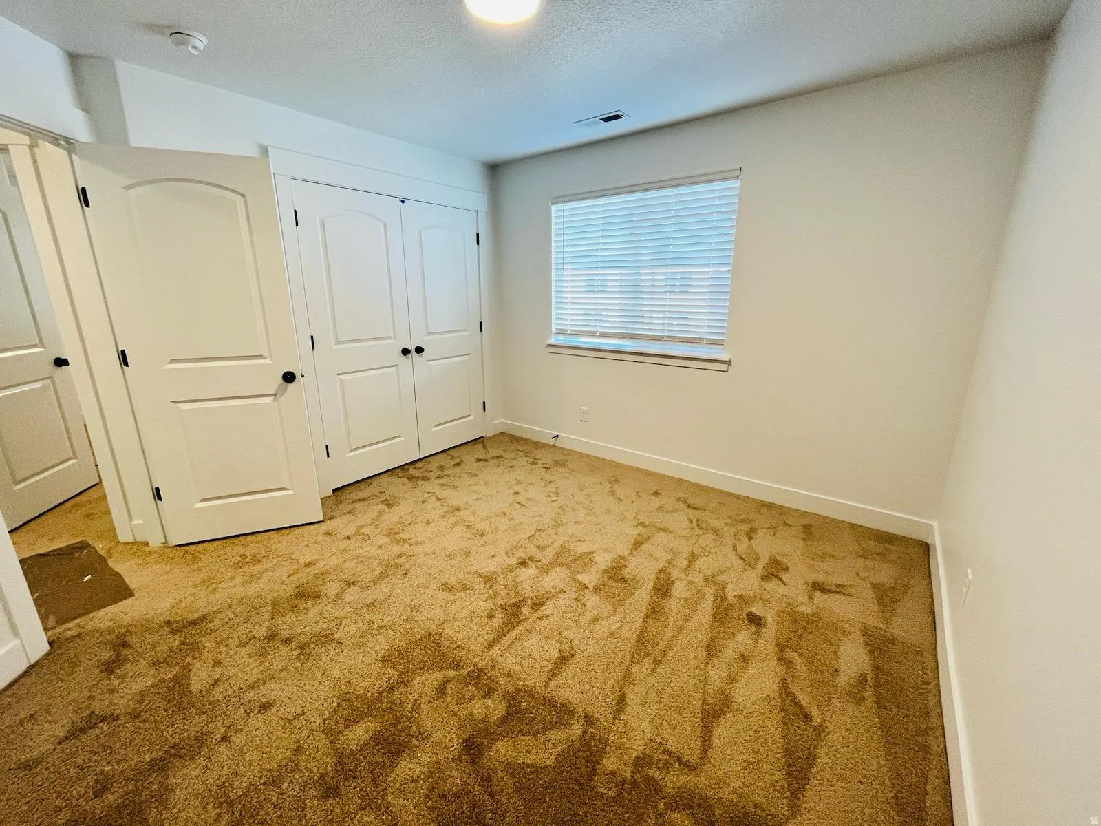 Carpeted interior room featuring white baseboards, a window with blinds, and white doors with black hardware