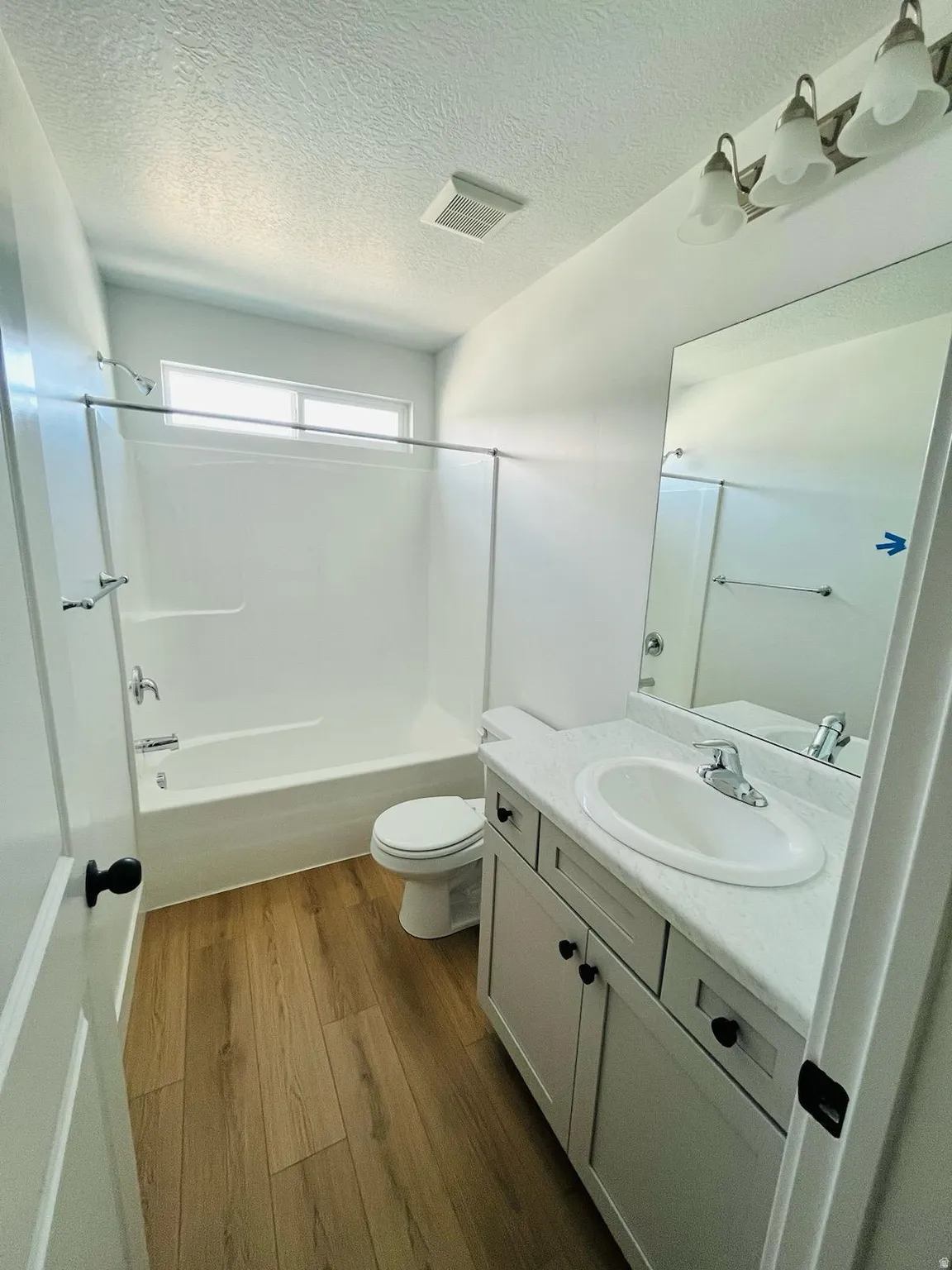 Bathroom featuring wood-finish flooring, a white vanity with an integrated sink, a large mirror, a white bathtub with a shower, and a translucent window