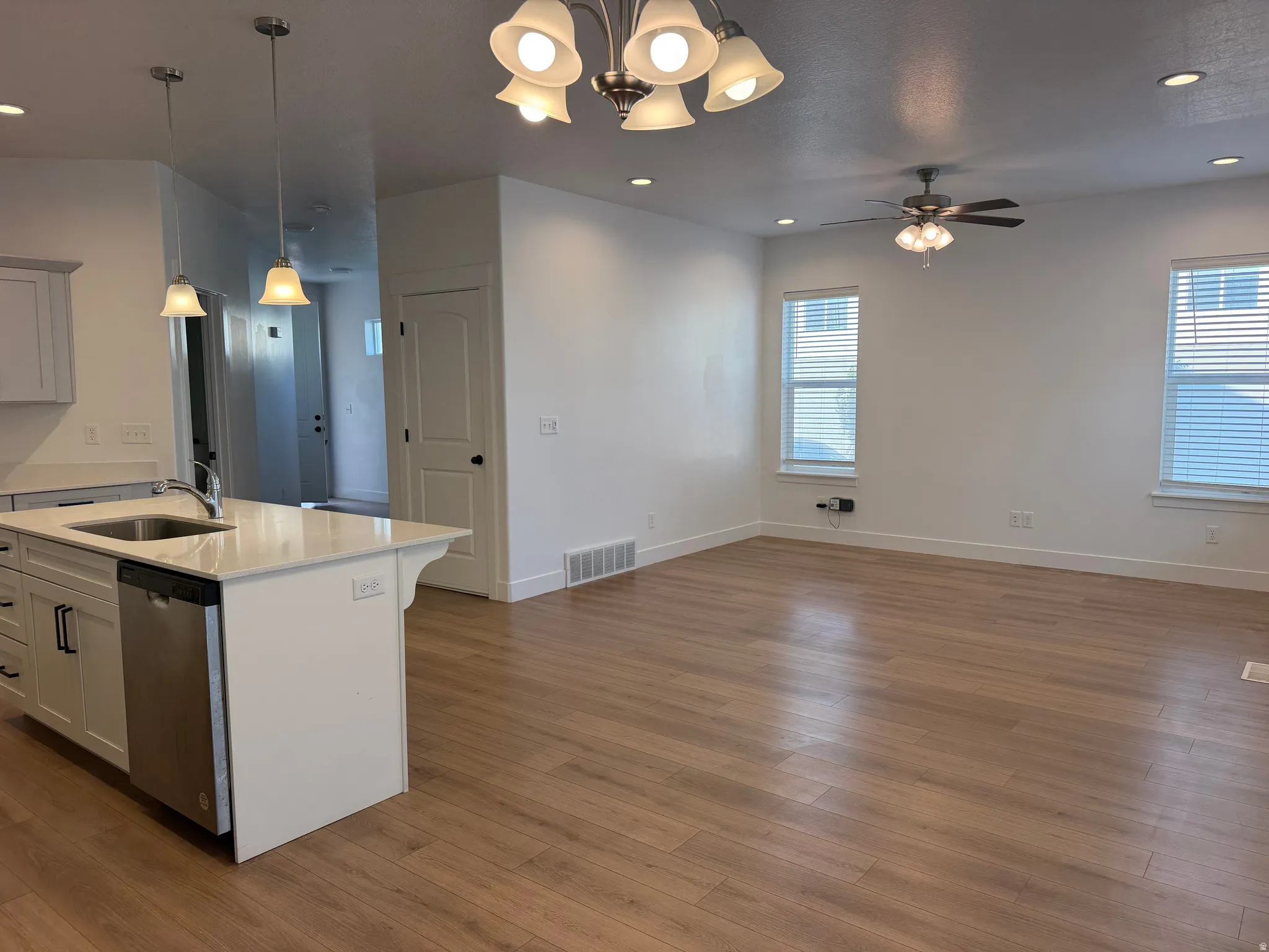 Open-concept living and kitchen area featuring stainless steel appliances, white cabinetry with black hardware accents, a quartz countertop island with waterfall edge, and hardwood flooring throughout