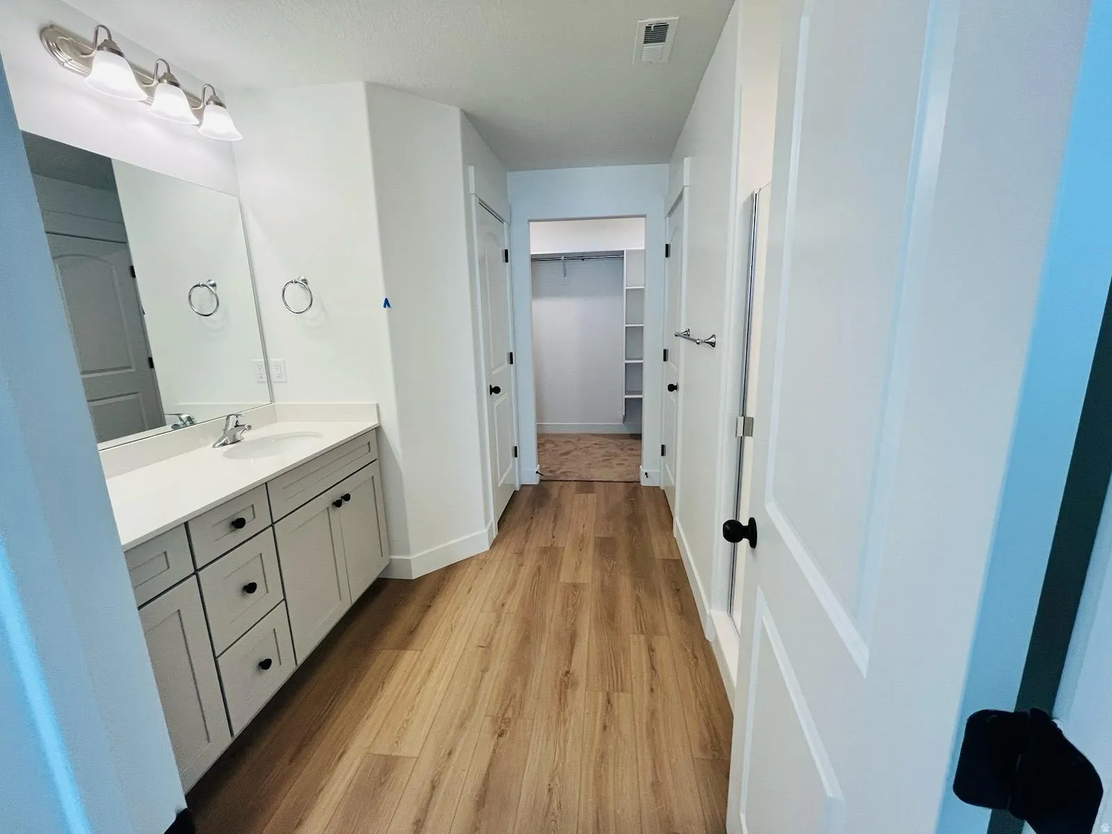 Bathroom vanity with a white countertop and coordinating cabinetry, featuring wood-finish flooring