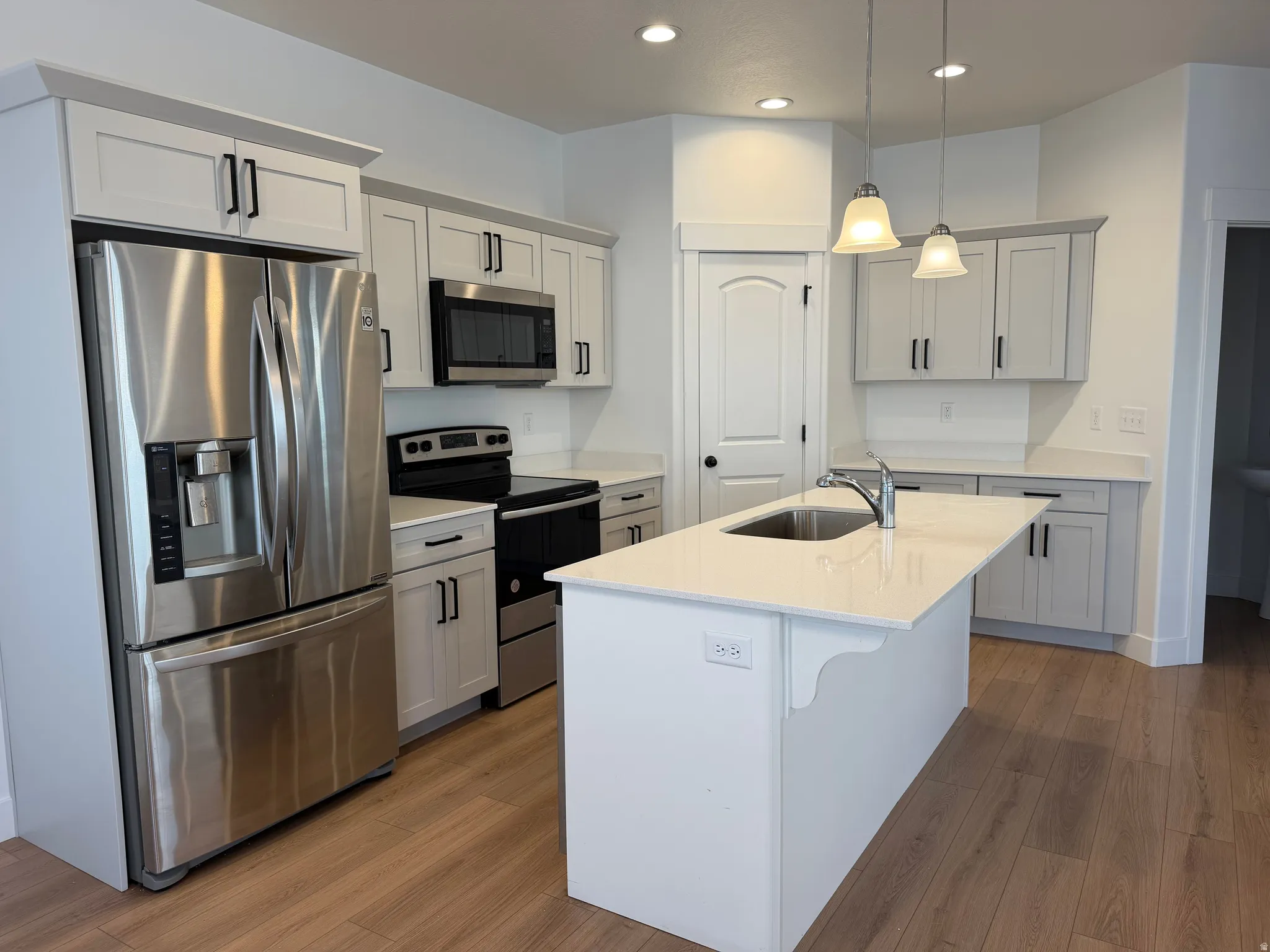 Kitchen featuring light-finish cabinetry, stainless steel appliances, recessed lighting, and a center island with an undermount sink and pendant lighting