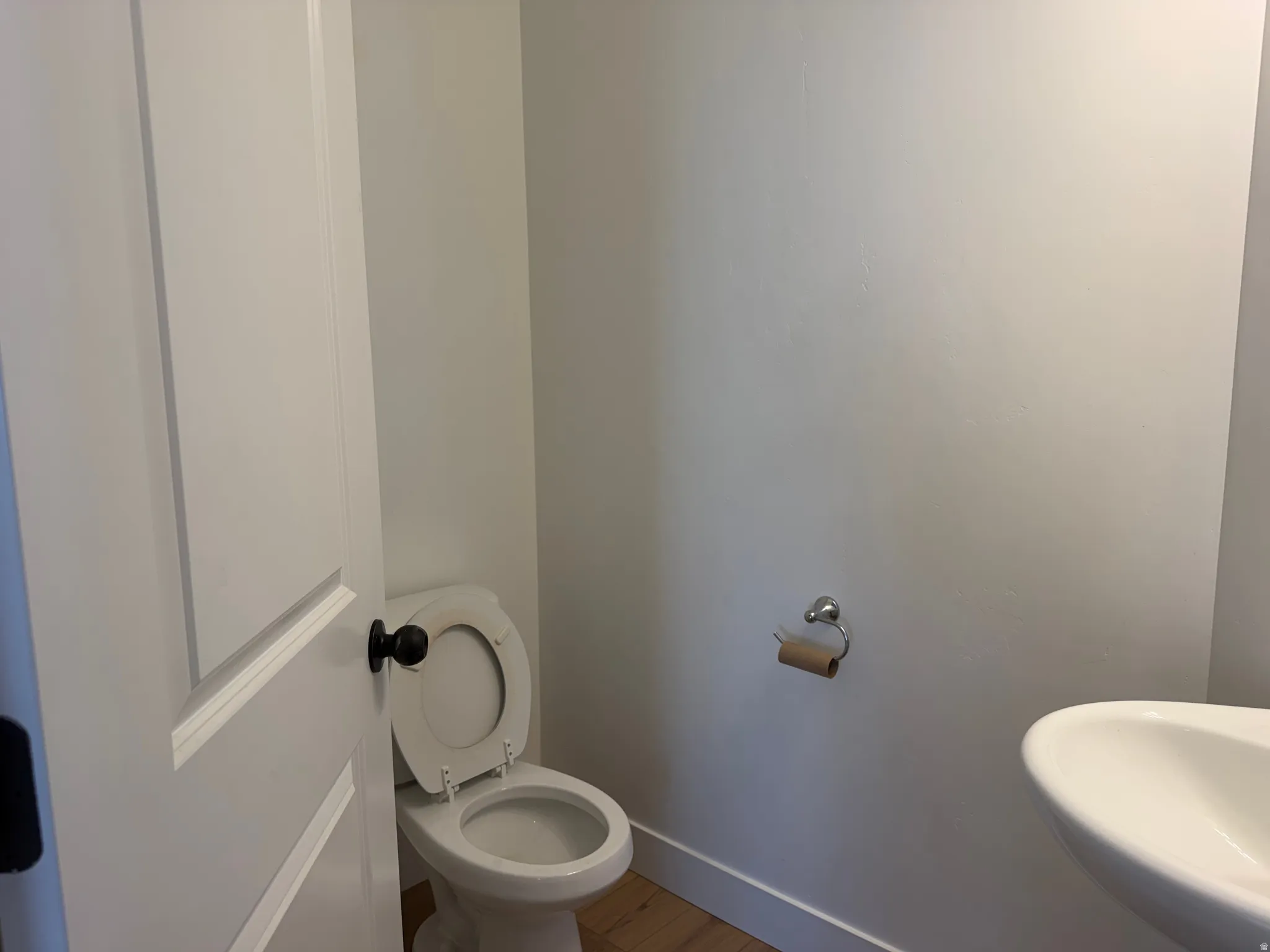 White paneled door with a black doorknob, white toilet, and a wall-mounted white sink with a chrome faucet