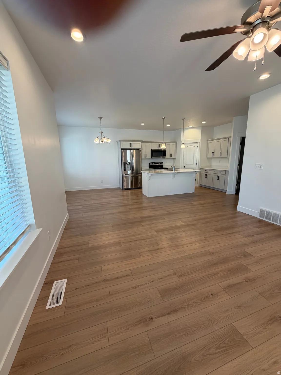 Open-concept living area featuring wood-finish flooring, a kitchen with light-toned cabinetry, stainless steel appliances, and a central island