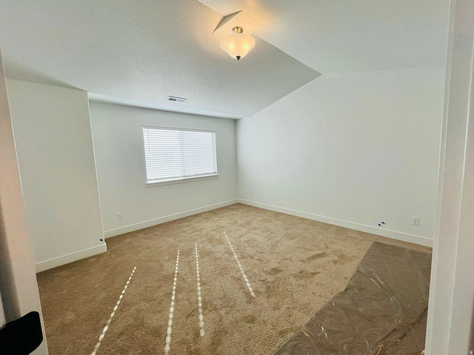 Spacious room featuring neutral carpeting, white baseboards, a single window with blinds, and a semi-flush mount ceiling fixture