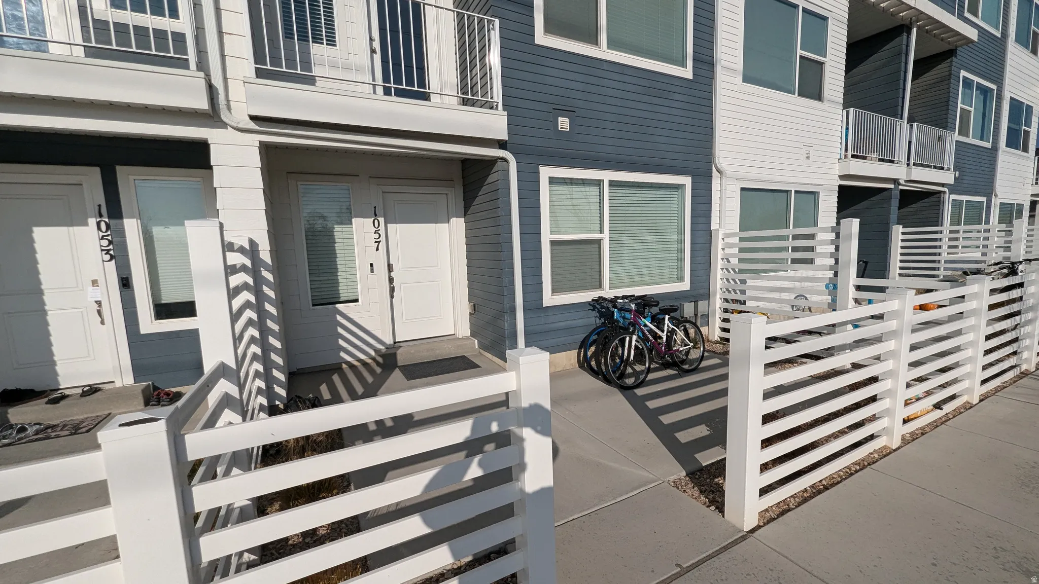 Multi-level residential building featuring a blue and white facade, ground-level entryways, and upper-story balconies with railings