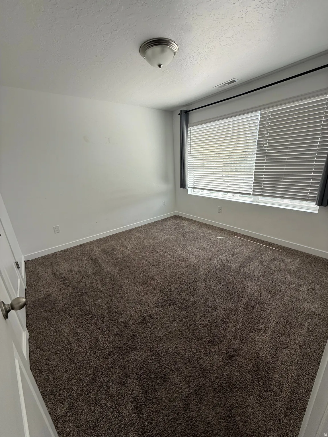 Bright interior space featuring a window with horizontal blinds, recessed baseboards, and plush dark carpeting