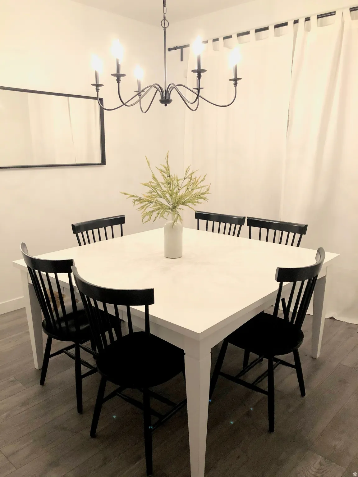 Dining area featuring a matte black chandelier with candle-style lights, white walls, and wood-finish flooring