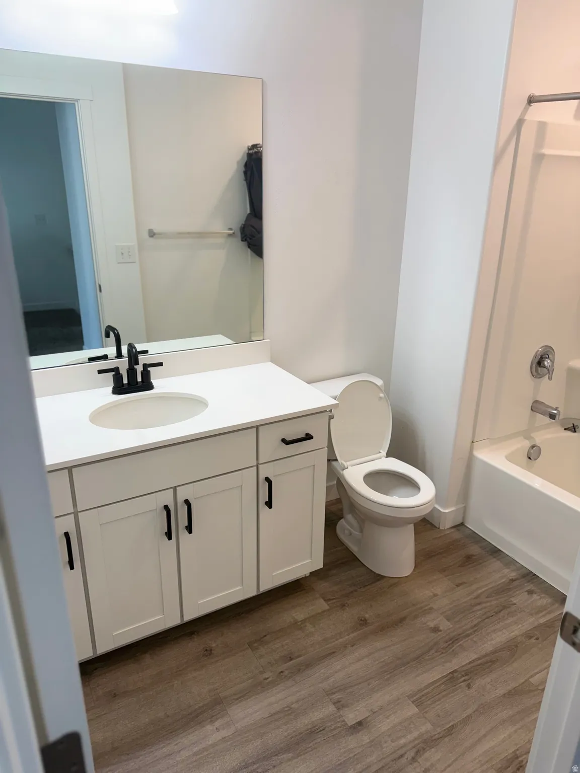 Bathroom featuring wood-finish flooring, a white vanity with shaker-style cabinetry, a white countertop, and a built-in bathtub with shower