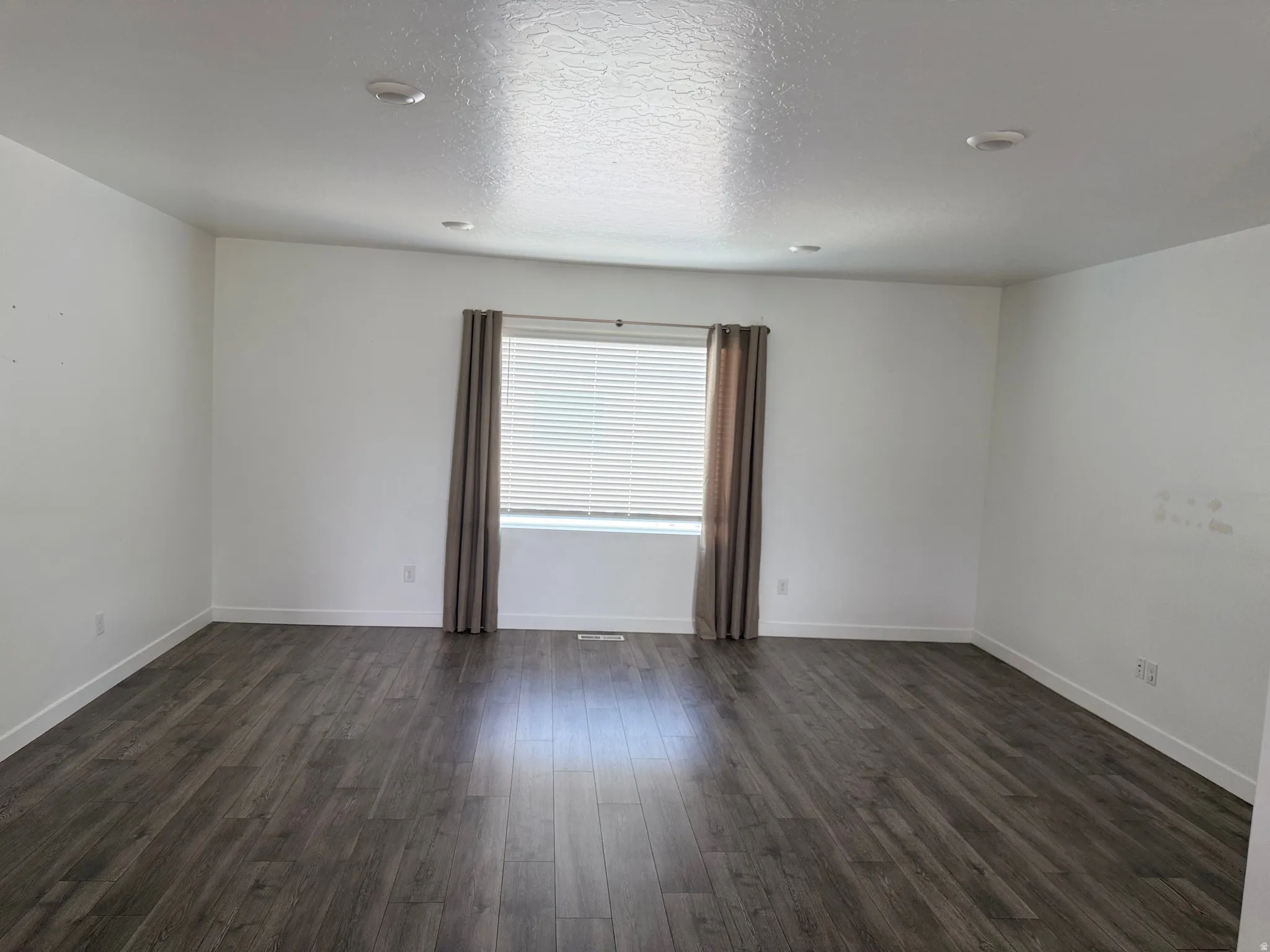 Spacious room featuring wood-finish flooring, recessed lighting, a window with blinds, and neutral wall tones