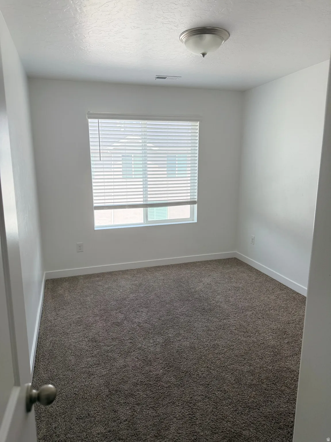 Room with neutral-toned carpeting, white walls, and a window with horizontal blinds