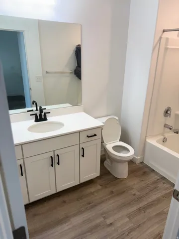 Bathroom featuring wood-finish flooring, a white vanity with shaker-style cabinetry, a white countertop, and a built-in bathtub with shower