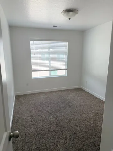 Room with neutral-toned carpeting, white walls, and a window with horizontal blinds