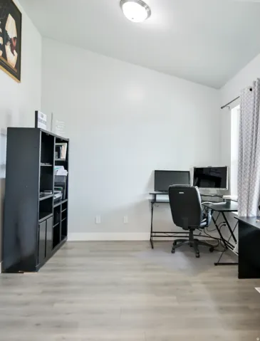 Vaulted ceiling with a flush-mount light fixture, light wood-finish flooring, white baseboards, and window with patterned drapes