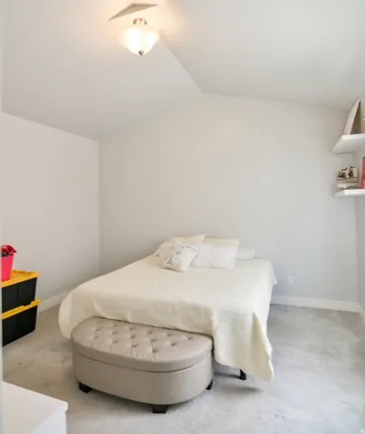 Bedroom featuring light gray walls, textured carpeting, and a sloped ceiling with a flush-mount light fixture
