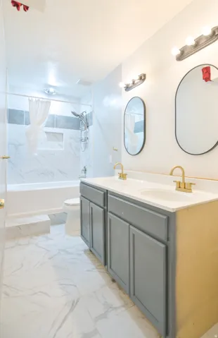 Bathroom featuring a double vanity with gray cabinetry, white countertops, and gold-finish fixtures