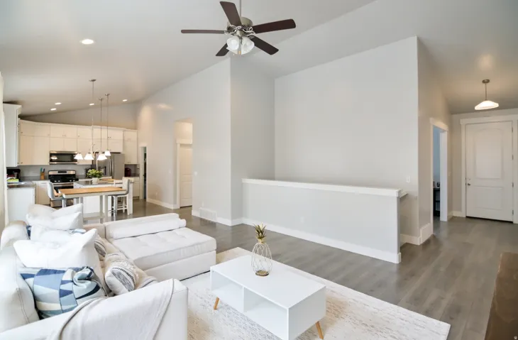 Open-concept living area featuring high vaulted ceilings with a ceiling fan, light wood-finish flooring, and a half-wall partition