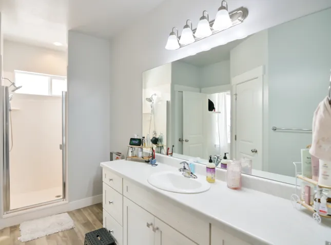Spacious bathroom featuring a white vanity with multiple drawers and cabinets, a single integrated sink, and an expansive mirror