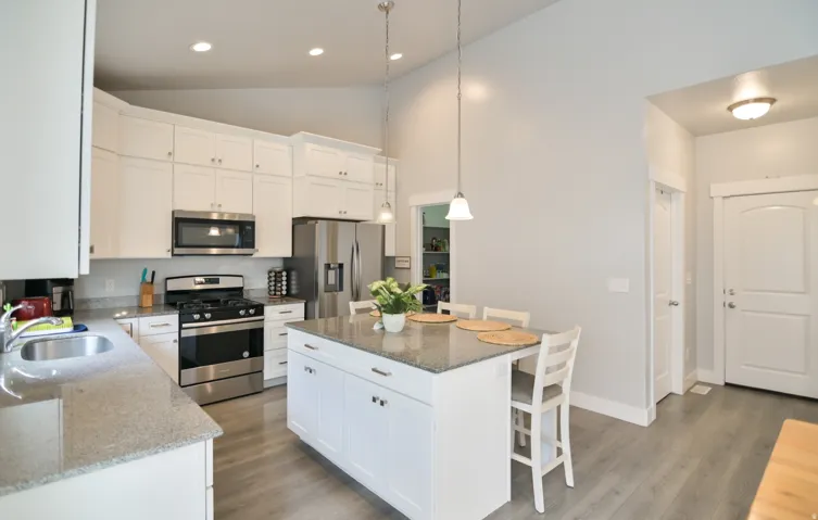Kitchen featuring white cabinetry, stainless steel appliances, granite countertops, an island with seating, and wood-finish flooring