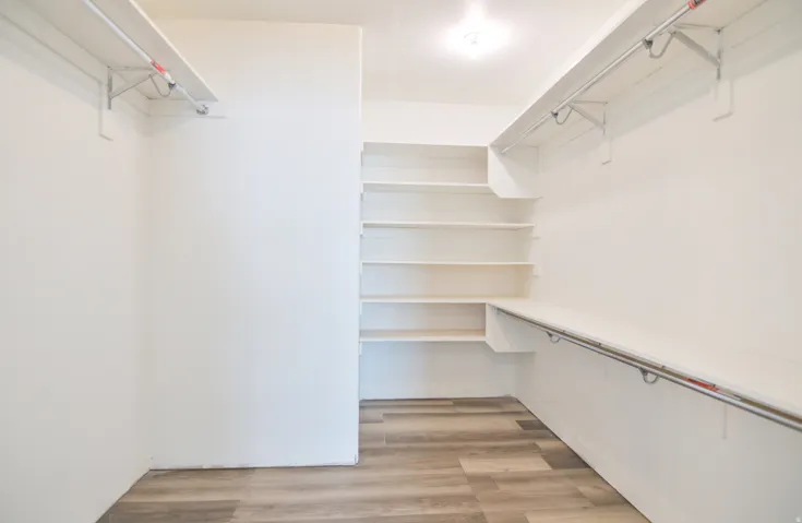 Walk-in closet featuring light wood-finish flooring, white walls, built-in shelving, and multiple hanging rods