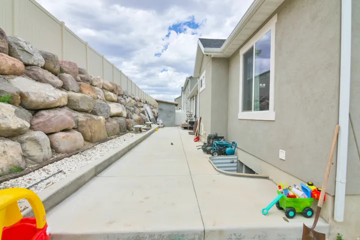 Side yard featuring a concrete pathway and a large rock retaining wall
