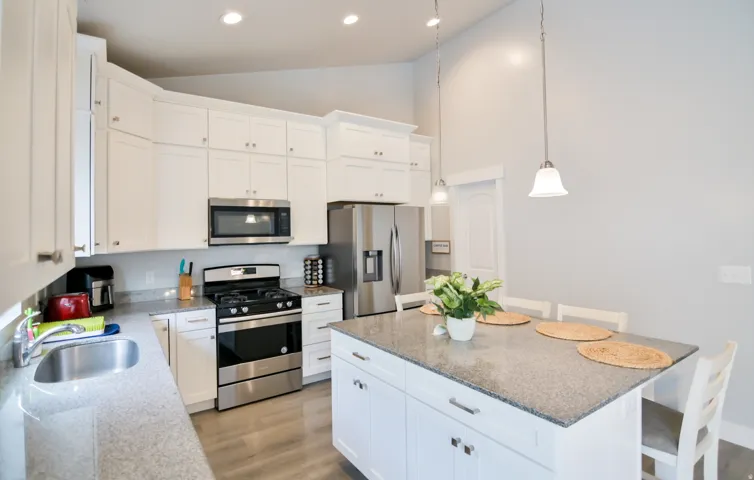 Kitchen featuring white shaker-style cabinetry, stainless steel appliances, granite countertops, and wood-finish flooring