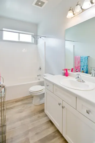 Bathroom featuring a white vanity with a single basin sink, light wood-finish flooring, white bathtub/shower combination, and a horizontal window
