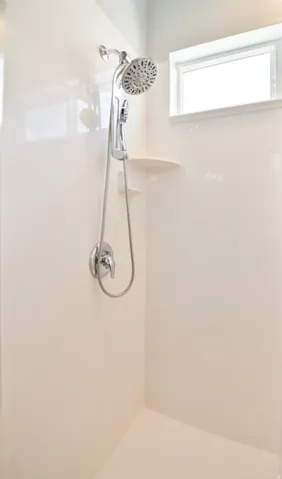 White shower enclosure featuring a multi-function showerhead with a handheld attachment, polished chrome fixtures, integrated corner shelving, and a high-set window