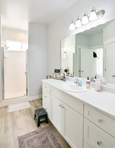 Contemporary bathroom featuring an elongated white vanity with a single integrated sink, a large mirror, and a glass-enclosed shower with a transom window