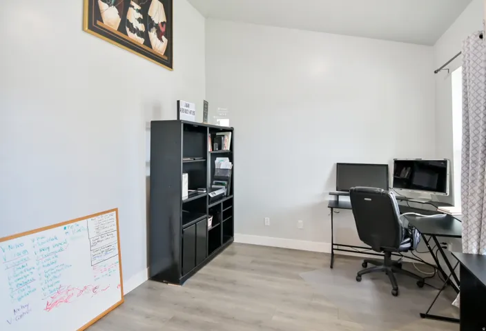 Bright interior room with light gray walls, wood-finish flooring, and a large window with patterned curtains