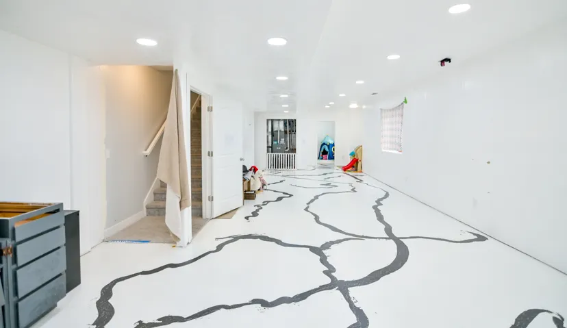 Spacious interior featuring a neutral color palette, recessed lighting, and a white painted floor with a unique dark gray pattern