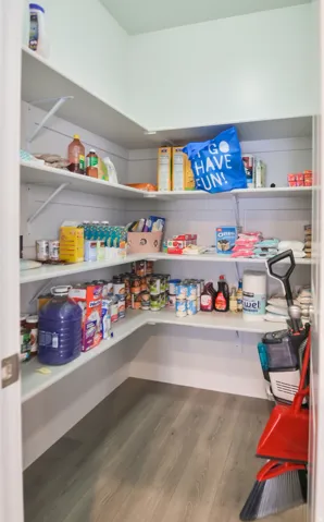 Walk-in pantry featuring abundant white shelving, wood-finish flooring, and light-toned walls