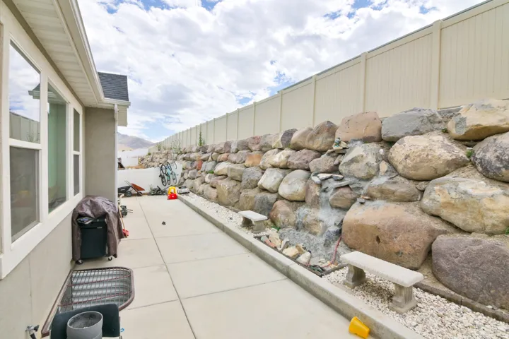 Paved side yard featuring a large rock retaining wall, privacy fence, and concrete pathway