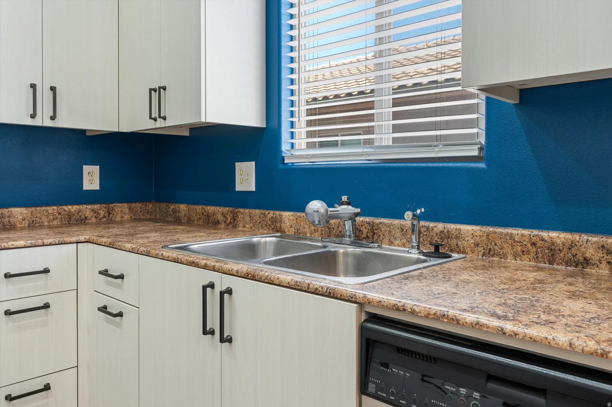 Kitchen featuring a stainless steel double-basin sink, light-toned cabinetry with dark hardware, and speckled countertops