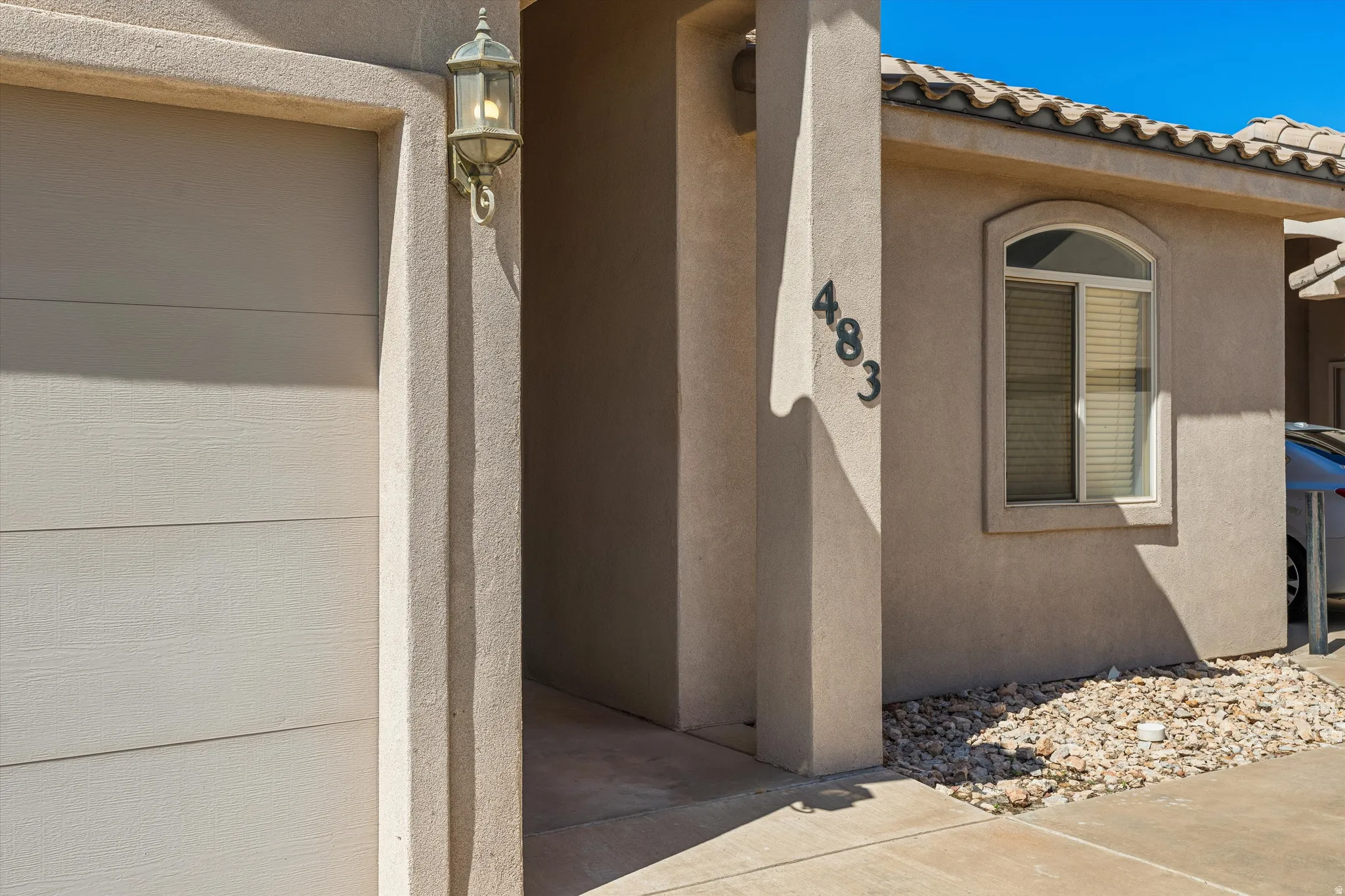 Stucco exterior featuring an arched window, decorative house numbers, and an attached garage with a panel door